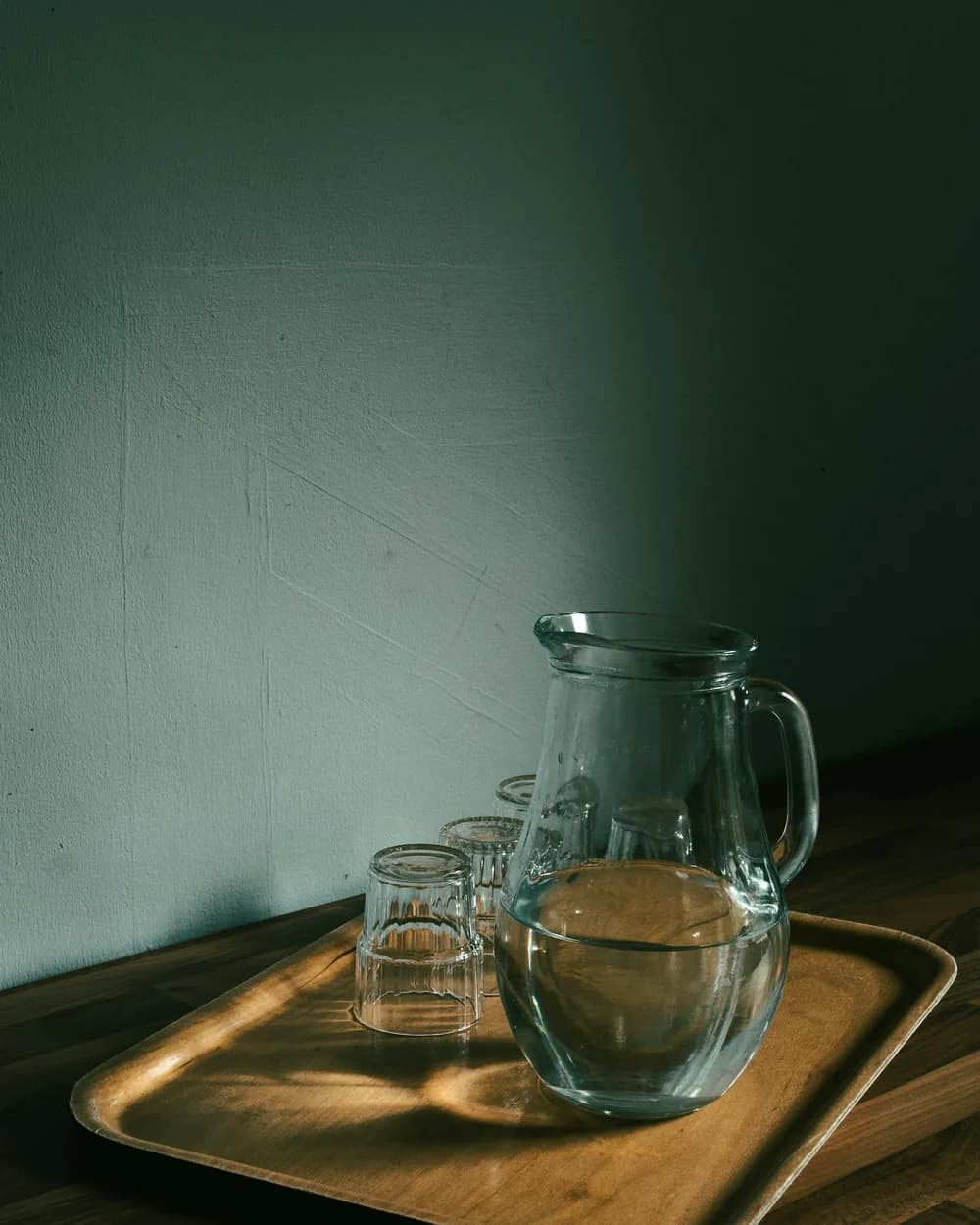 A glass water jug and tumblers on a wooden tray